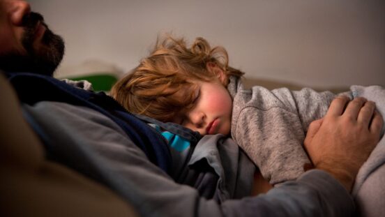 Curly haired toddler boy lying down and sleeping on his dad's chest