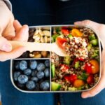 Lunch box spolit into three sections with blueberries, nuts, and a quinoa salad