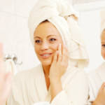 Mum and daughter wearing towels on their head, looking in the mirror and putting cream on their skin