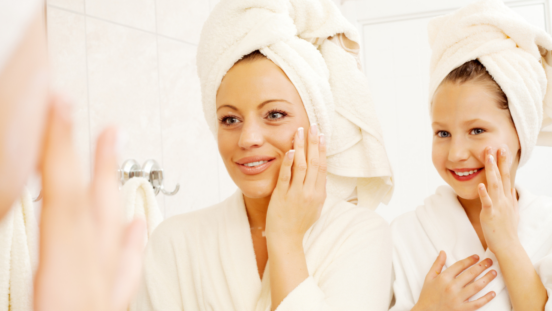 Mum and daughter wearing towels on their head, looking in the mirror and putting cream on their skin