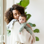 Women with dark curly hair holds dark haired baby over her shoulder to wind him