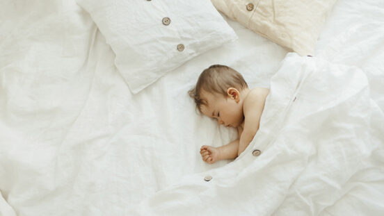 Peaceful baby lying on a white natural linen bed while sleeping in a bright room.