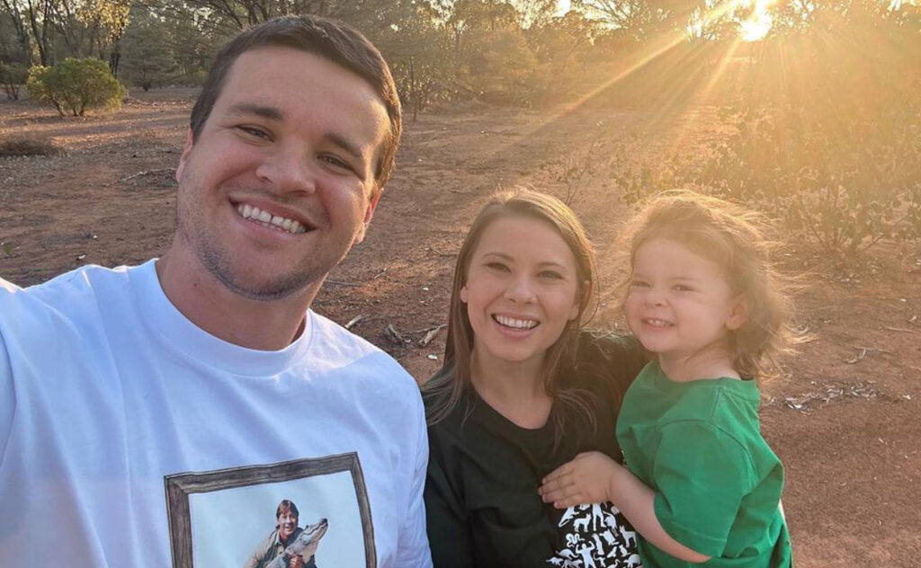 Chandler Powell, Bindi Irwin and Grace Warrior smile at the camera while the sun sets behind them.