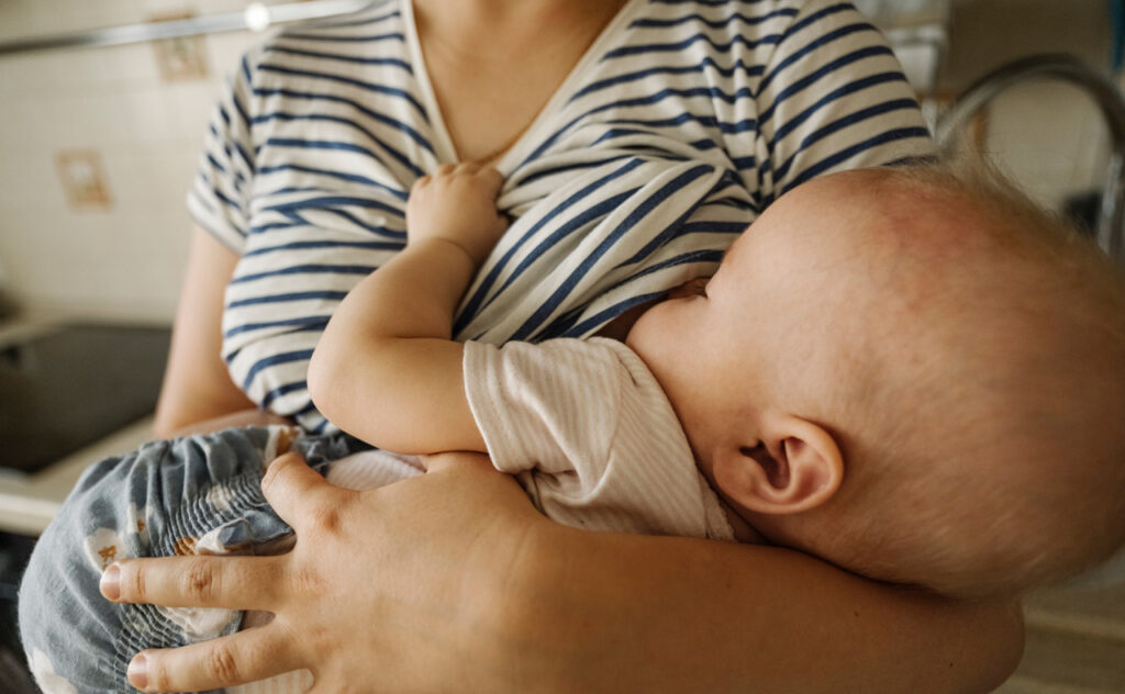 Mother's carrying toddler and breastfeeding at home.