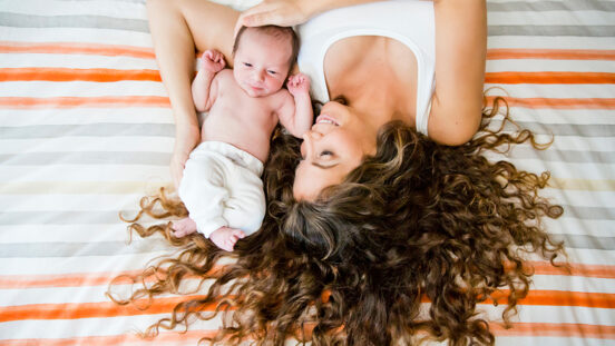 Stylised portrait of mother with curly hair holding newborn baby.