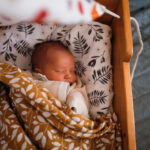 Newborn baby sleeps in wooden hanging retro cradle with muslin diapers. Top view.