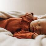 Sleeping newborn baby girl wearing rust coloured onesie.