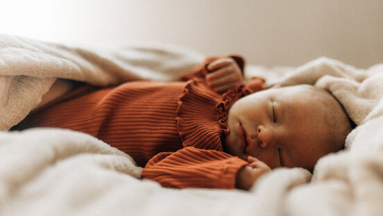 Sleeping newborn baby girl wearing rust coloured onesie.