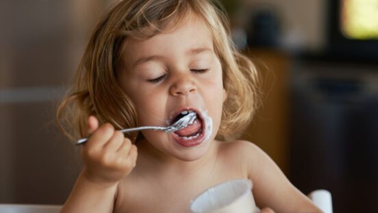 Blonde hair toddler girl eating yoghurt with her eyes closed