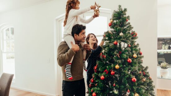 Girl on father's shoulders placing star on top of Christmas tree