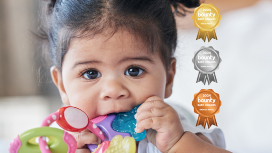 Close up of dark haired baby girl chewing on a colourful teething toy