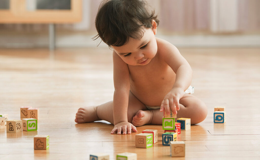 Small dark haired toddler playing with alphabet blocks.