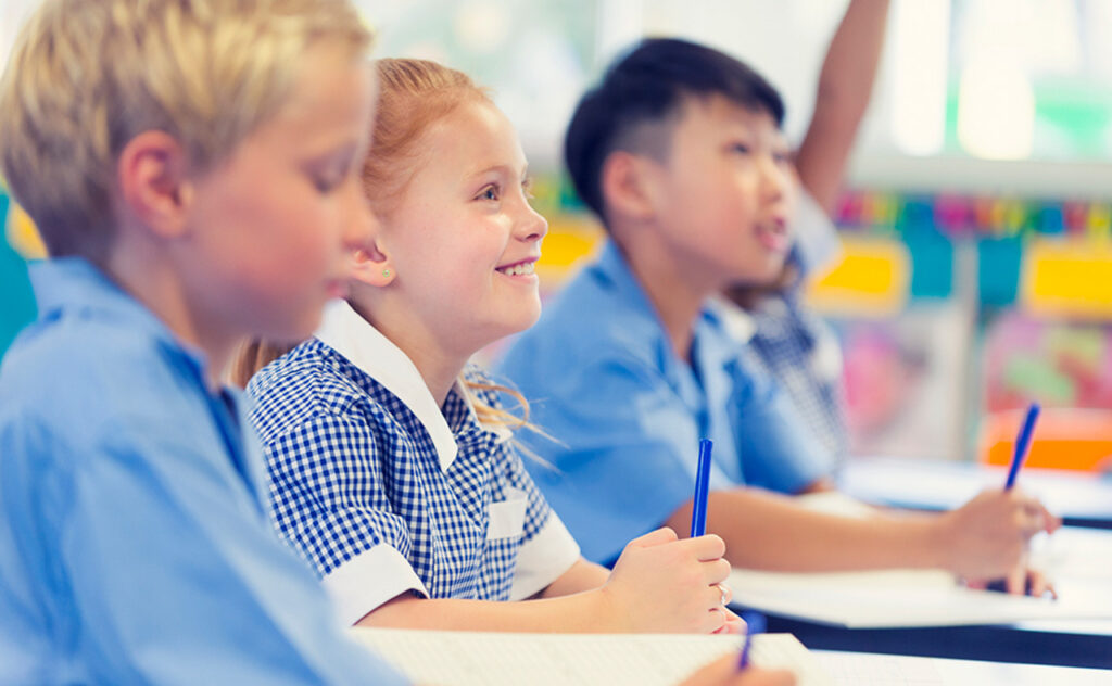 Group of children listening to the teacher. They are in a classroom. Multiethnic group with Caucasian and Asian kids. School girl is smiling and happy.