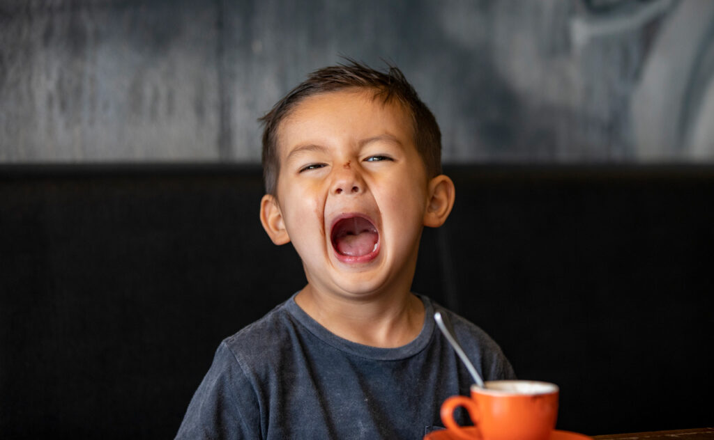 A close up shot of a 4 year old boy looking at camera pulling a sad face.