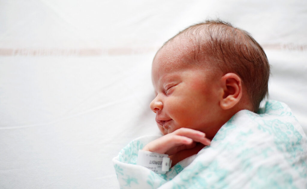 Side profile of a newborn baby wrapped in a hospital blanket in the maternity ward.