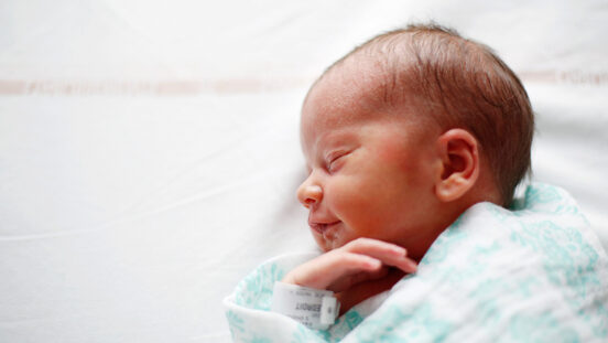 Side profile of a newborn wrapped in a hospital blanket at maternity ward.