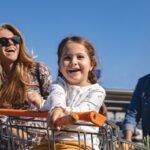 Young family with one child, having fun at the parking lot, playing with shopping cart