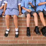 Children in school uniform sitting on a wall, heads not visible