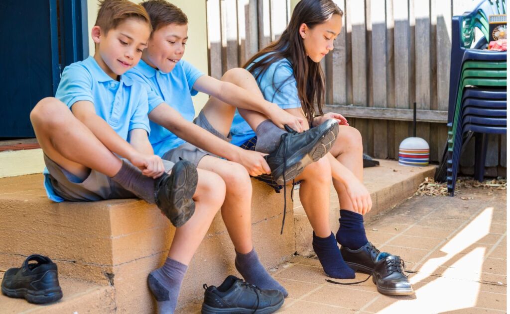 Three children in school uniform putting on their school shoes