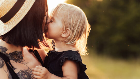 Closeup portrait of mother and little daughter playing together in summer park on sunset lights.