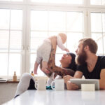 Young tattoed mother and father with newborn baby sitting in their kitchen and having fun together