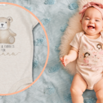 Smiling baby in headband and cute body suit, lying on rug next to cardigan and leggings