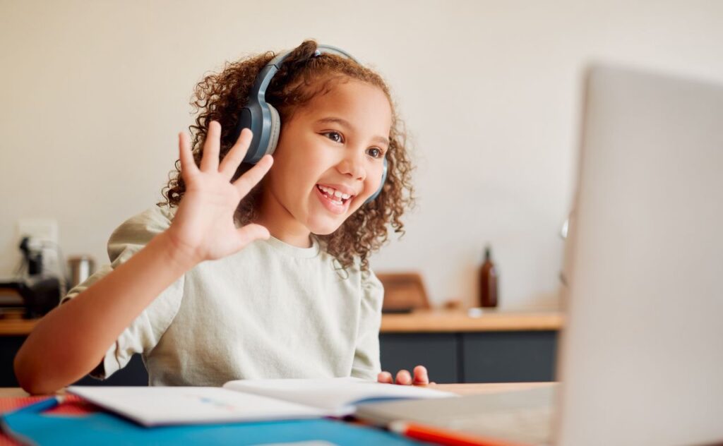 Girl with headphones on and waving at laptop screen