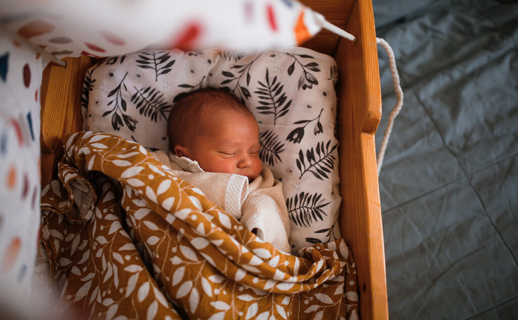 Wrapped newborn baby sleeps in wooden hanging retro cradle with muslin