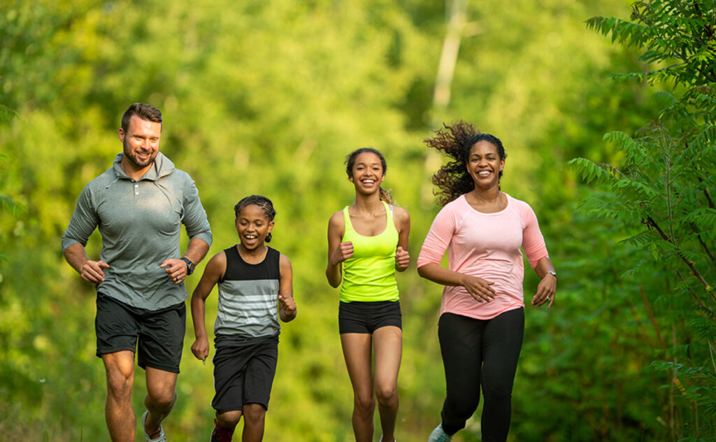 A multi-ethnic family (mother, father, son, daughter) getting exercise by going for a jog at the park.
