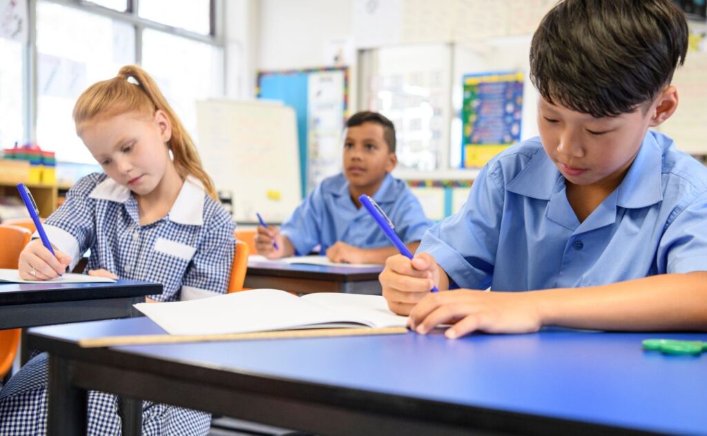 Asian boy in blue shirt with other pupils sitting in classroom doing their school work