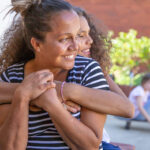 mothers day gift ideas - Mother and daughter with curly hair embracing at home in Australia