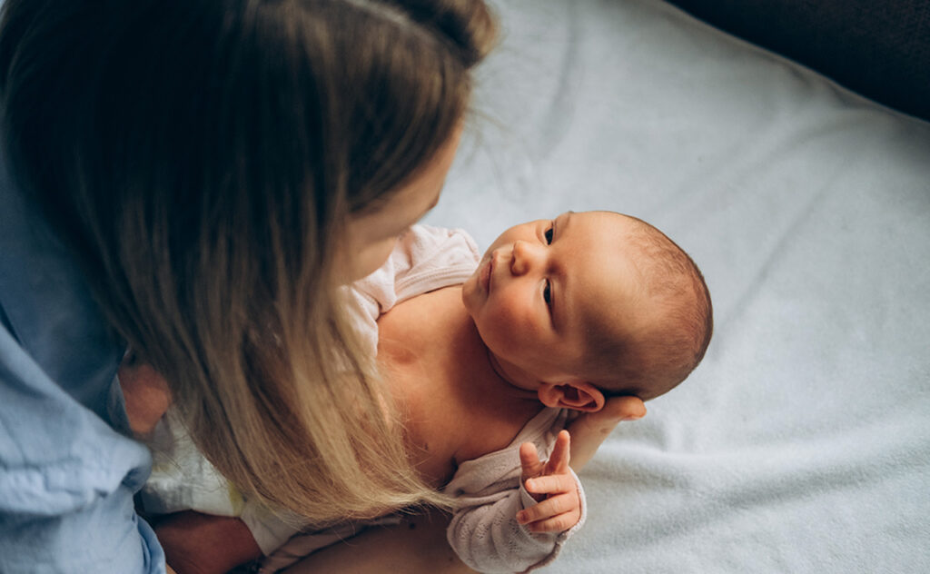 Mother making eye contact with alert newborn as she gets them dressed.