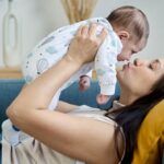 Woman holding and kissing her baby while lying on the sofa.