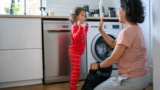 Eurasian three year old girl who is wearing pajamas gives her mom a high-five after helping her do the laundry at home.