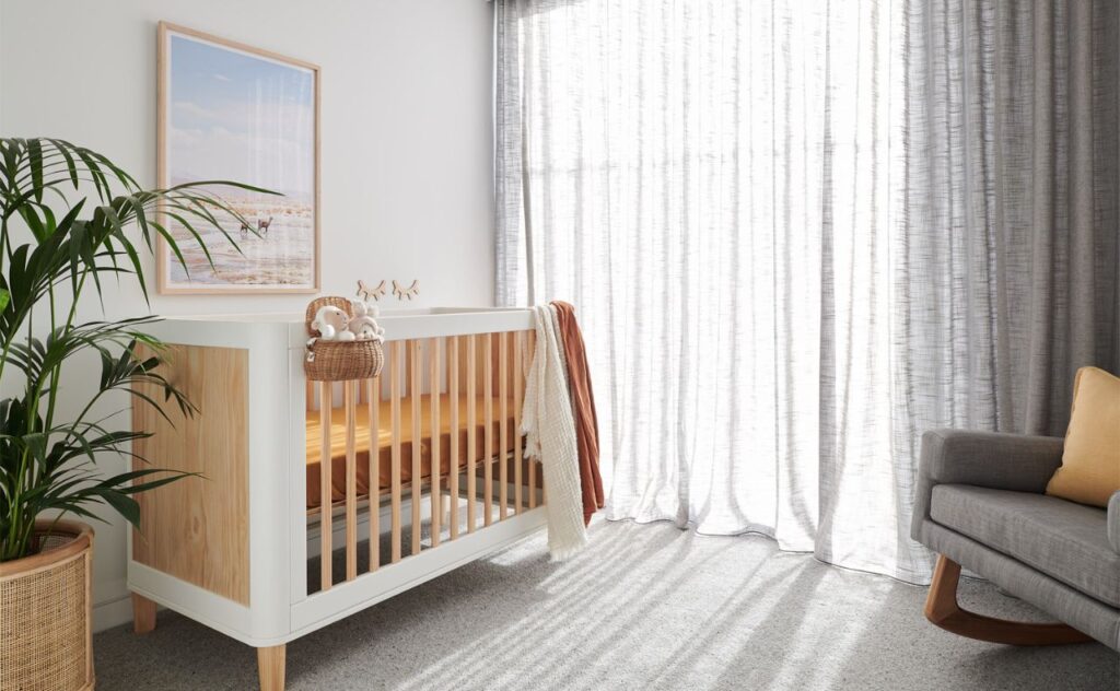 Cosy baby's nursery with a white and wooden cot, sheet curtains and an armchair