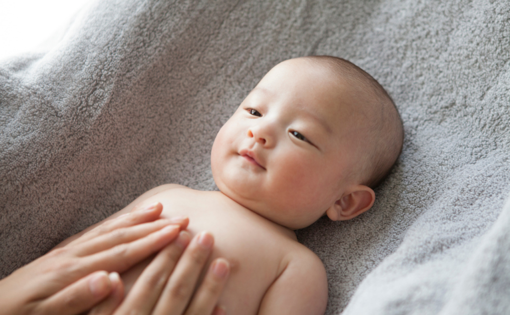 Close up of Asian baby with two hands on their chest giving them skin to skin baby massage