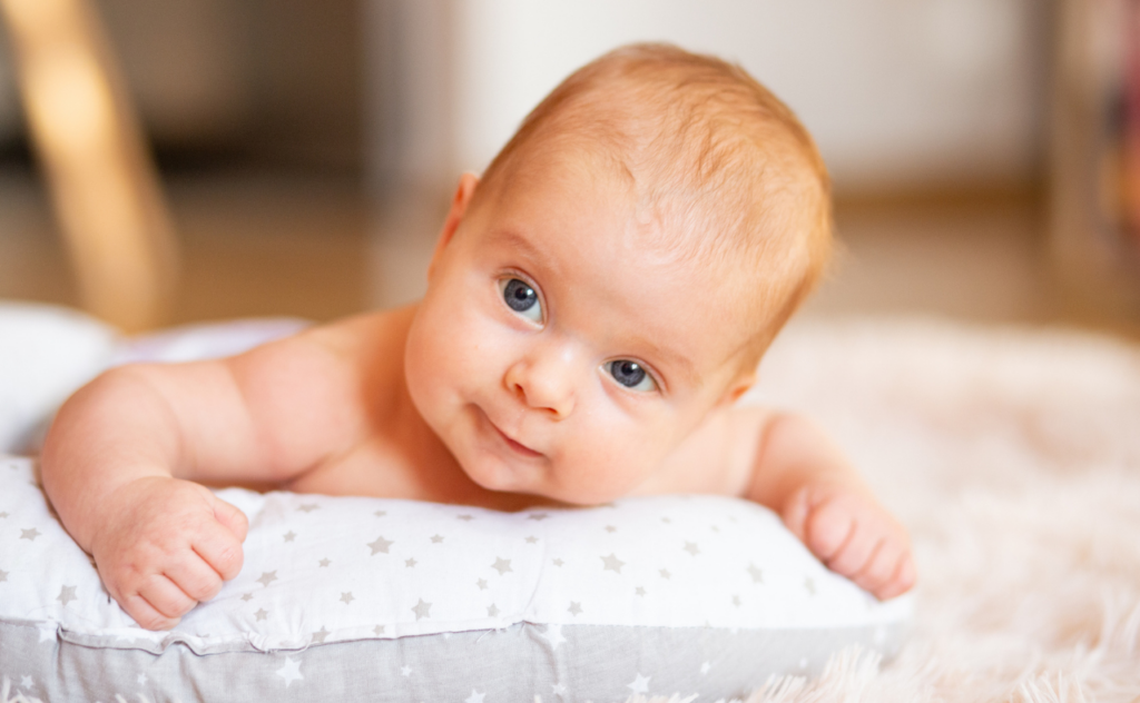 Baby with blue eyes and light red heair on their tummy, head raised