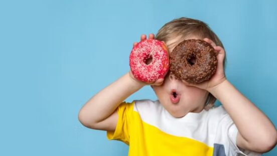 Young boy holding two donuts over his eyes