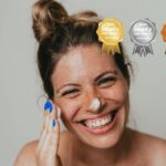 Happy freckled woman applying moisturising cream on face