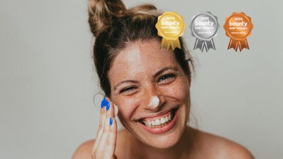 Happy freckled woman applying moisturising cream on face