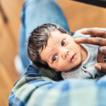 High angle view of cute newborn in father's arms at home. Close-up of a man holding son in living room.