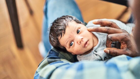 High angle view of cute newborn in father's arms at home. Close-up of a man holding son in living room.