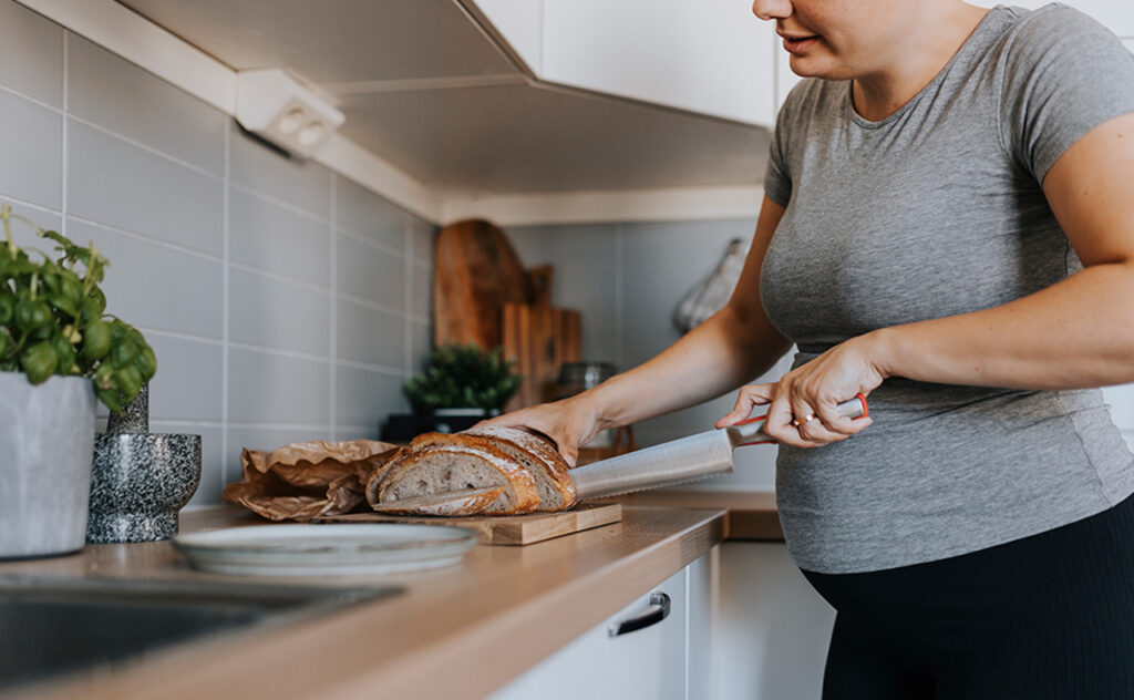 Pregnant woman slicing bread to prepare meal