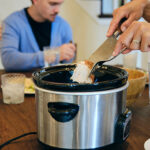 A multiracial family eating dinner in their home. Mum serves dinner from slow cooker.