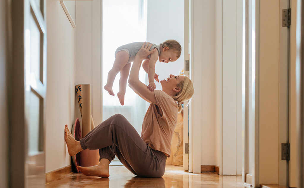 Side view of playful young woman lifting baby daughter. Cute toddler girl is having fun with mother. They are enjoying at home.