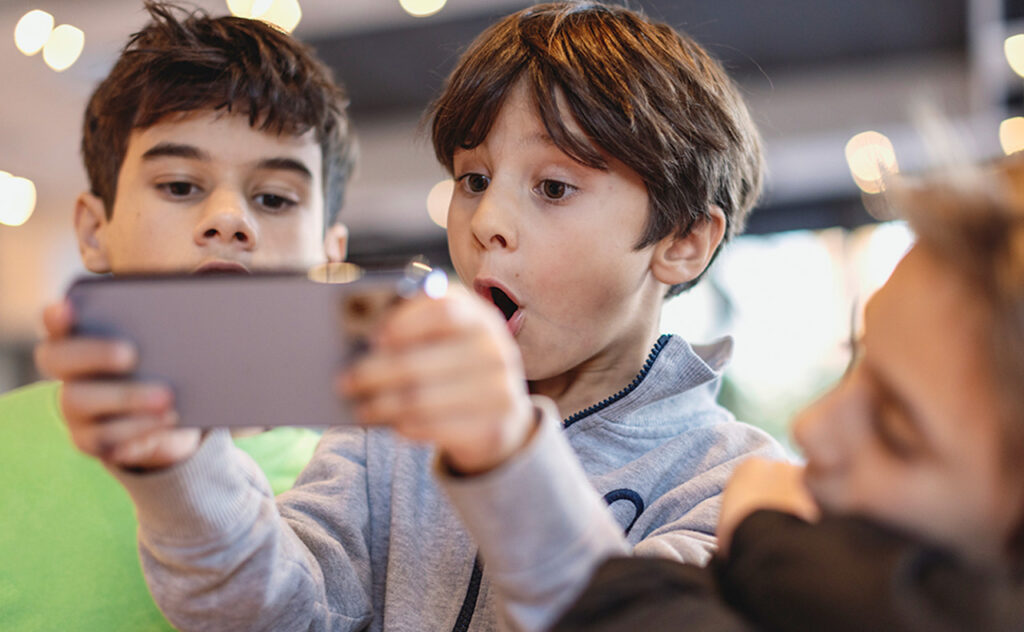 Kids sitting on a table, in a restaurant, using a smartphone