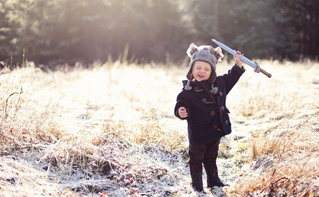 Little girl in field, dressed as a Viking and holding a toy sword in the air