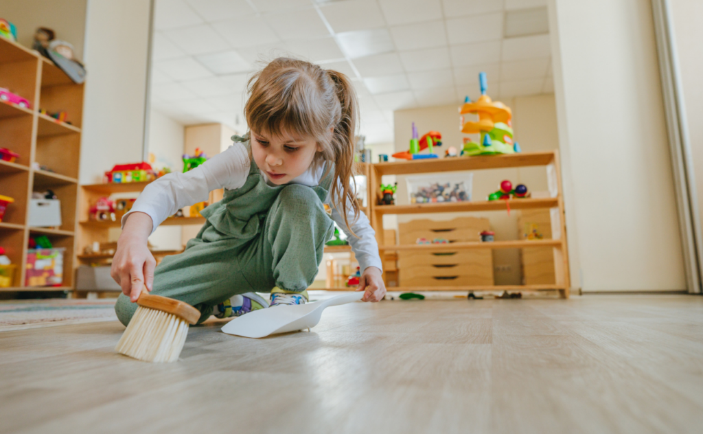 Preschool girl crouching down and using a toy-sized dustpan and brush