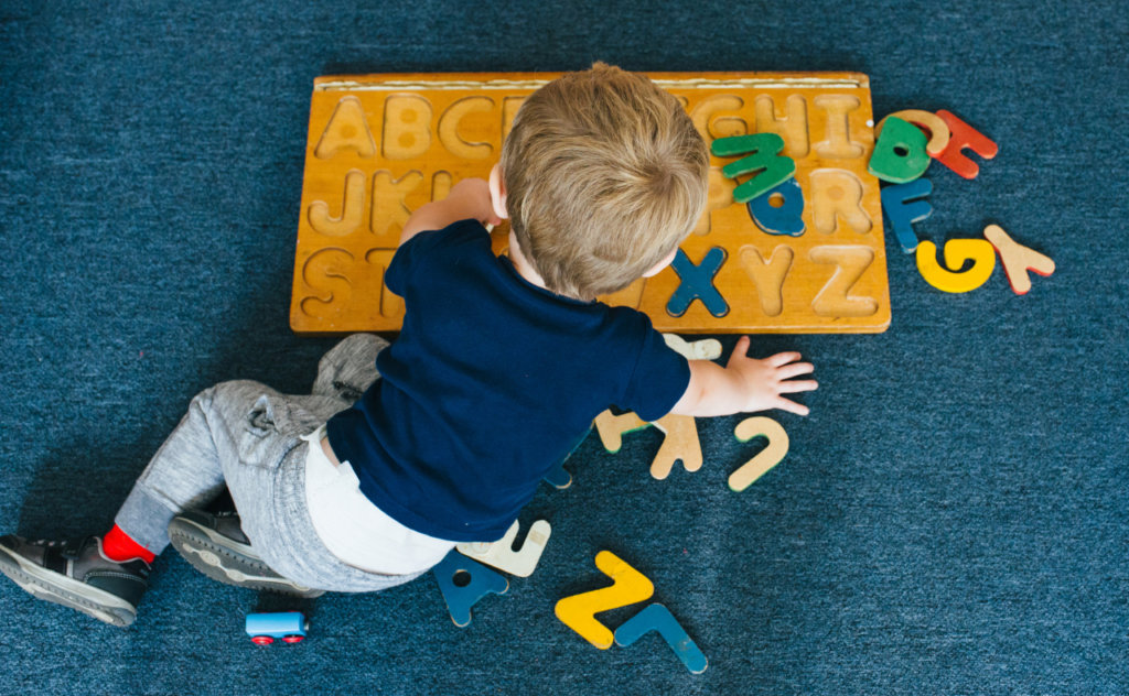 Aerial view of toddler boy playing with large wooden alphabet puzzle on a blue mat