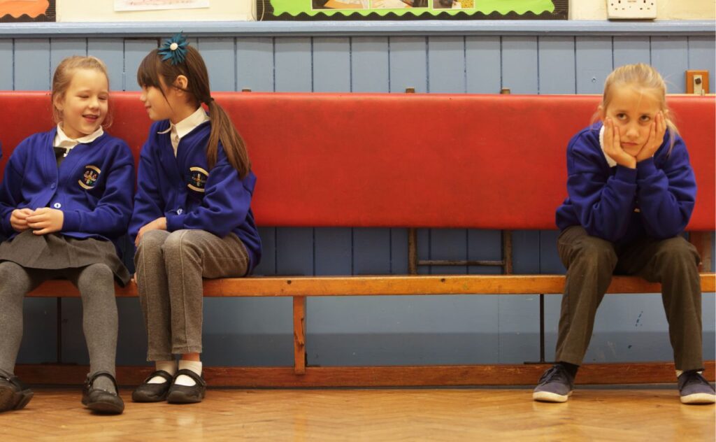 Girls in school uniform sitting on a bench with one girl being left out and bullied